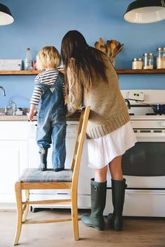 a woman standing next to a little boy on top of a chair in a kitchen