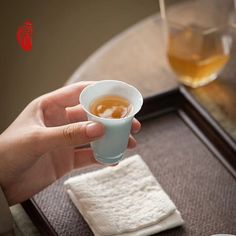 a person is holding a cup of tea on a tray with two cups in front of them