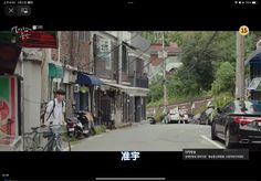 a man riding a bike down a street next to tall buildings and parked cars in front of them