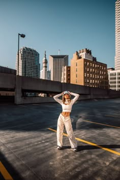 a woman standing in the middle of an empty parking lot with her arms behind her head