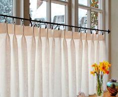 a vase with yellow flowers sitting on a table next to a window covered in white curtains