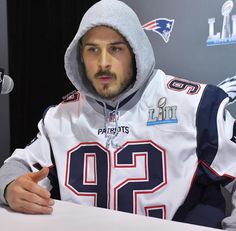 a man wearing a hoodie sitting at a table with a microphone in front of him