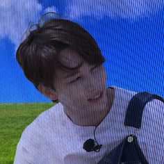 a young man wearing headphones while sitting in front of a television screen with grass and blue sky behind him