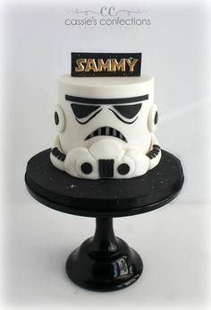 a star wars themed cake is on a black stand with white frosting and gold lettering