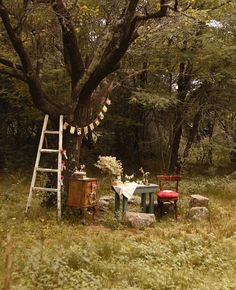 a table and chair under a tree in the woods with bunting flags on it