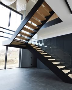 a modern staircase with glass railing and wood handrails in an empty room next to a large window