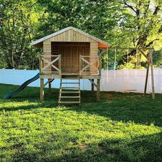 a small wooden structure in the grass with a slide next to it and a fence behind it