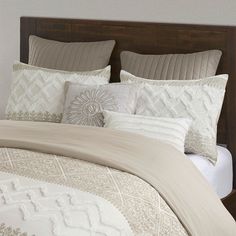 a bed with white and beige comforters and pillows on top of it in a bedroom