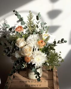 a vase filled with white flowers and greenery on top of a wooden crate next to a wall