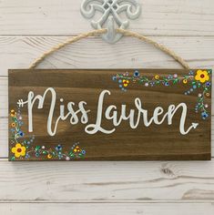 a wooden sign that says miss lauren hanging on a white wood wall with flowers around it