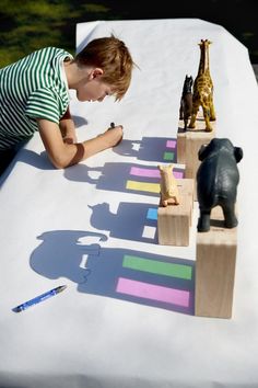 a young boy is playing with wooden animals on a long white table outside in the sun