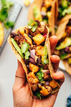 a person holding up a taco filled with meat and veggies on it