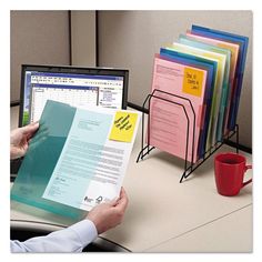 a man is holding a binder and working on his computer at the office desk