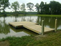 a wooden dock sitting in the middle of a lake surrounded by green grass and trees