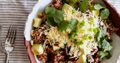 a white bowl filled with rice, meat and veggies next to a fork