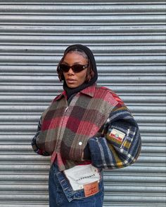 a woman standing in front of a garage door wearing a plaid jacket and jeans with her hands on her hips