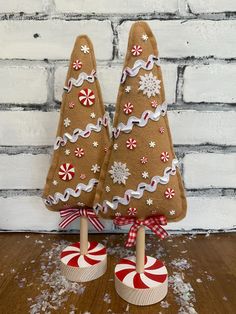 two christmas trees made out of felt on top of a wooden table next to a brick wall