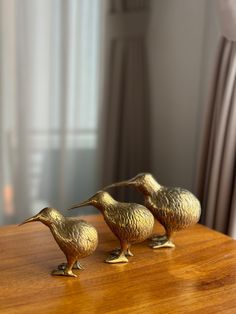 three brass birds sitting on top of a wooden table