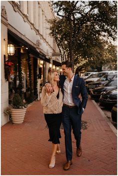 a man and woman are walking down the street in front of some buildings with christmas lights