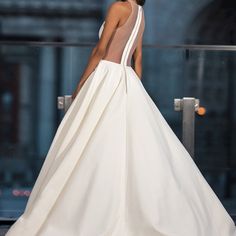 a woman in a white dress is walking down the runway with her back to the camera