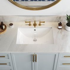 a bathroom sink with gold faucet and marble counter top under a round mirror