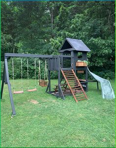 a wooden swing set with a slide and swings in the grass next to some trees