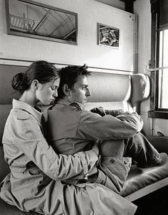 a man and woman are sitting on a bed looking at something in the distance with their arms around each other