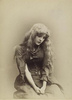 an old photo of a woman with long blonde hair sitting on the floor wearing a dress