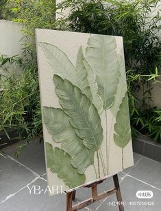 an easel with a painting on it in front of some plants