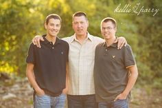 three men standing next to each other in front of trees