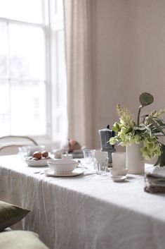 the table is set with plates, cups and flowers in vases on top of it