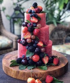 a three tiered cake with fruit on top and berries on the bottom, sitting on a wooden platter