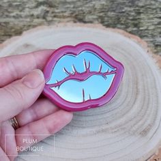 a hand holding a pink lip shaped mirror on top of a piece of tree trunk