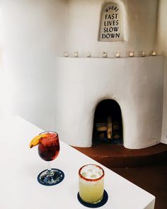 two drinks sitting on top of a white counter next to a fireplace in a room