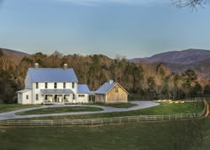 a large white house sitting on the side of a lush green field next to a forest