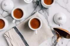 four cups of coffee sit on a marble table with spoons and teapots