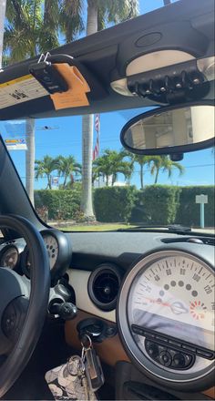 the interior of a car with steering wheel, dashboard and gauges in front of palm trees