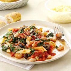 a white plate topped with pasta and spinach covered in sauce next to other dishes