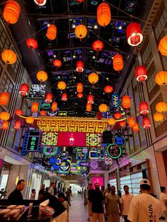 people are walking through an indoor shopping mall with lanterns hanging from the ceiling above them