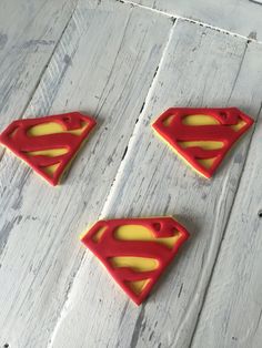 three plastic superman logo magnets sitting on top of a white wooden table next to each other