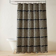 a black and white shower curtain hanging from a metal hook on a wooden floor next to a bathtub