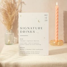 a table topped with a white sign next to a candle and vase filled with flowers