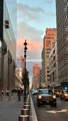 cars are driving down the street in front of tall buildings and skyscrapers at sunset