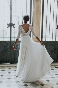 a woman in a long white dress is standing on a tiled floor with her back to the camera