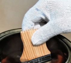 a gloved hand holding a wooden object in a can