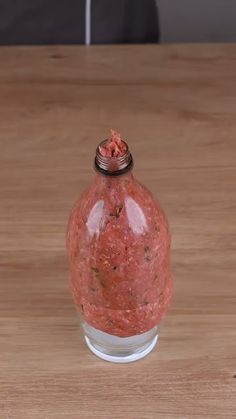 a glass bottle filled with red stuff sitting on top of a wooden table