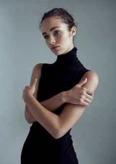 a woman with her arms crossed in front of her face, wearing a black dress