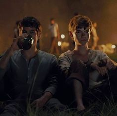 two people sitting in the grass with one holding a camera up to their face and another taking a photo