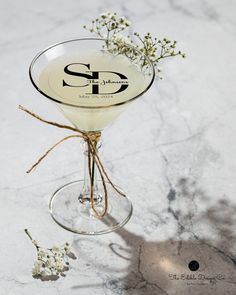 a glass filled with a drink sitting on top of a marble counter next to flowers