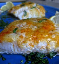 two pieces of fish on a blue plate with lemon wedges and parsley garnish